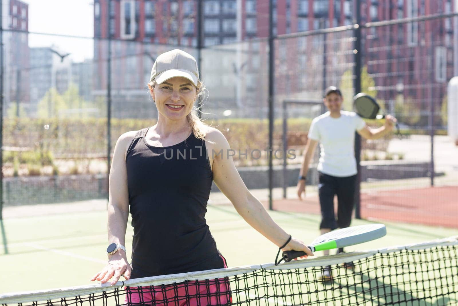 Portrait of positive young woman and adult man standing on padel tennis court, holding racket and ball, smiling. High quality photo