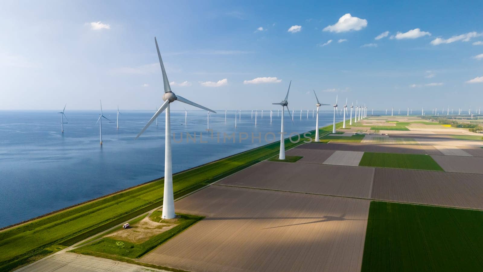 A mesmerizing aerial view of a wind farm in Flevoland, Netherlands, where windmill turbines rhythmically generate clean energy near the ocean.