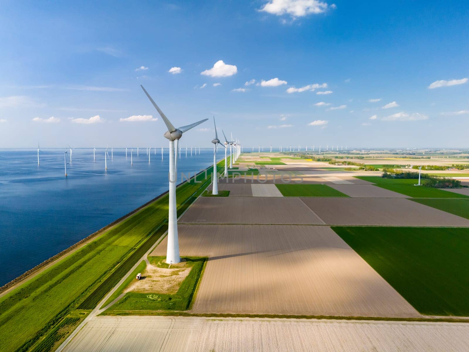A breathtaking aerial view captures a wind farm in the Netherlands Flevoland region, with rows of majestic windmill turbines gracefully turning near the ocean.