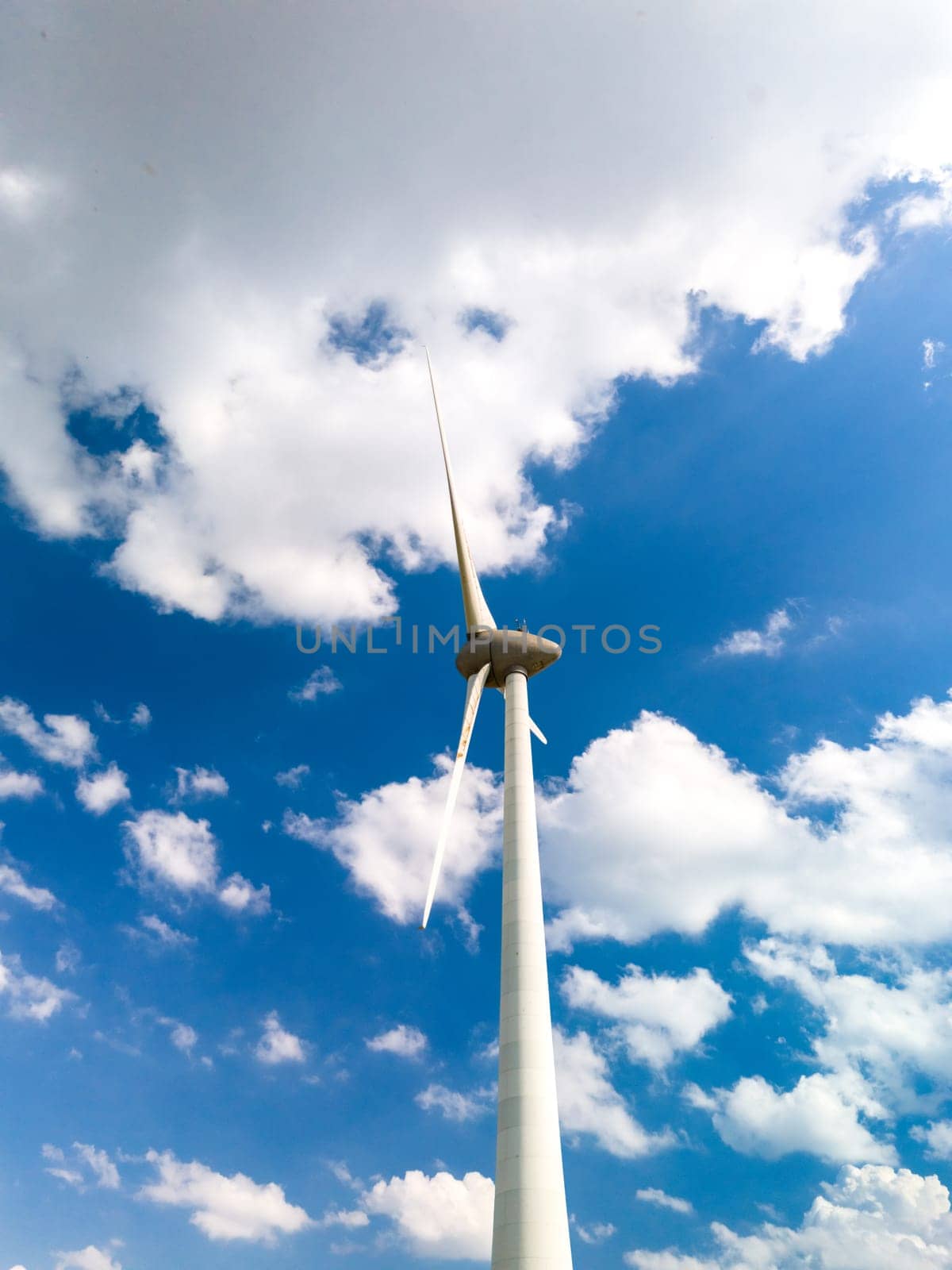 A tall wind turbine gracefully spins in the center of a clear, blue sky, harnessing the power of the wind in Flevoland, Netherlands by fokkebok