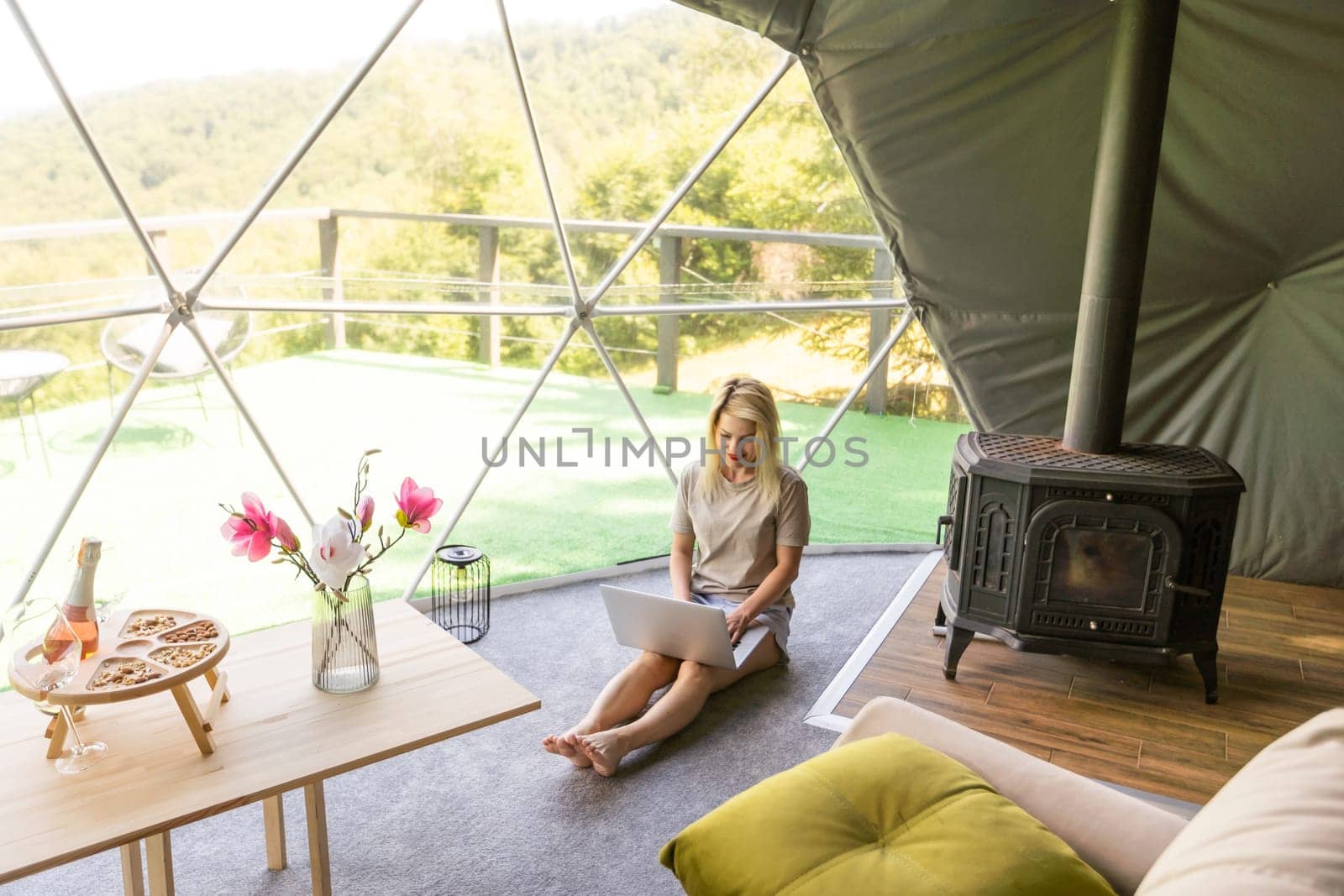 Transparent bubble tent at glamping, Lush forest around and interior. Woman with laptop.