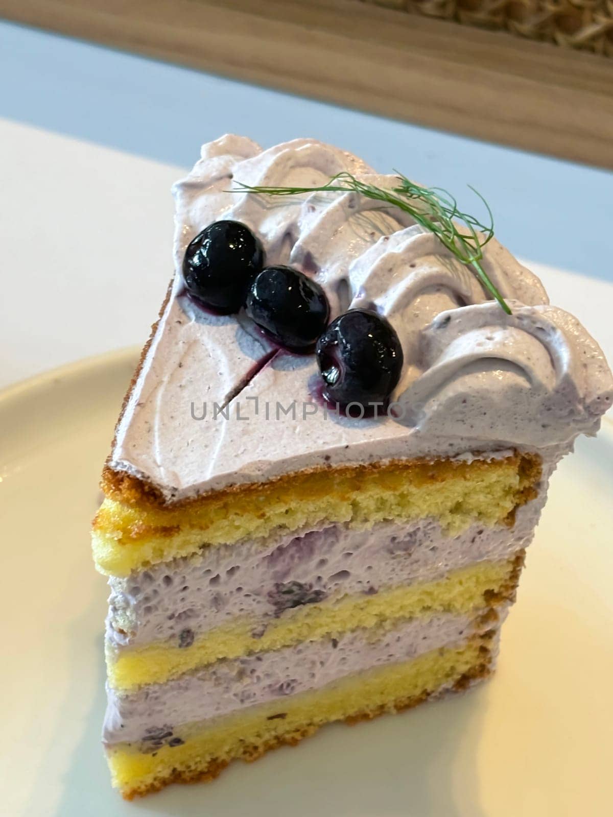 slice of blueberry cake decorated with fresh berries on white plate, delicious layered cake, top view in the cafe
