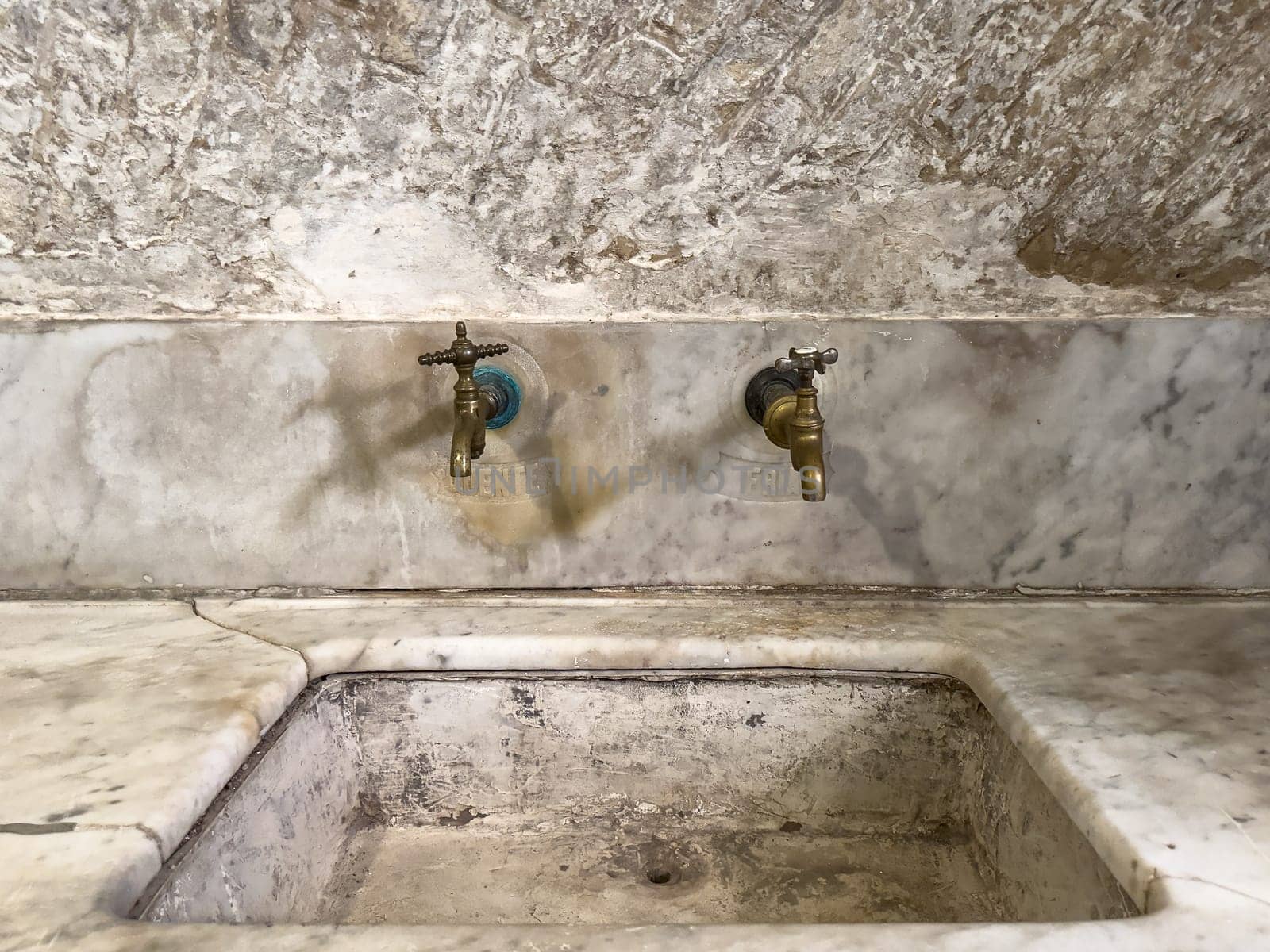 Aged marble sink with two brass taps, radiating historical charm and wear.