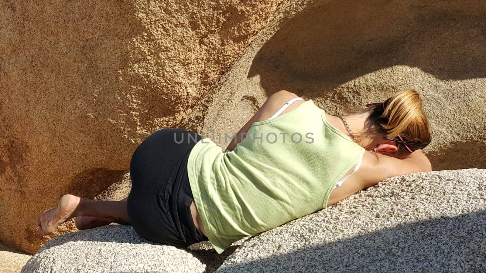 Back View of Fit Woman in Yoga Pants and Tank Top with Ponytail, Tired from Hiking, Laying on Boulders. High quality photo