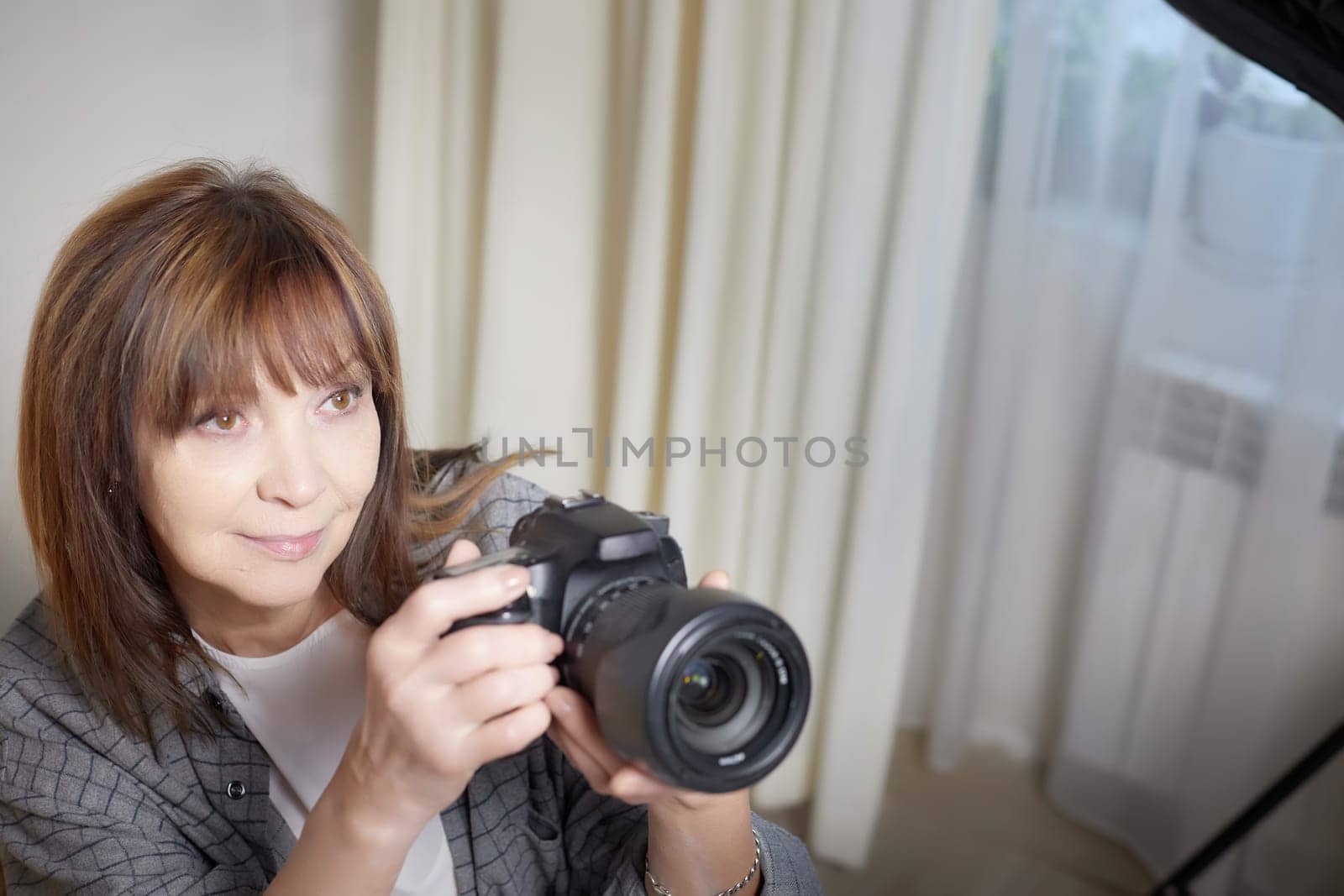 Senior old elderly woman with black camera with a large lens indoors in the studio. Professional photographer. Age Hobby