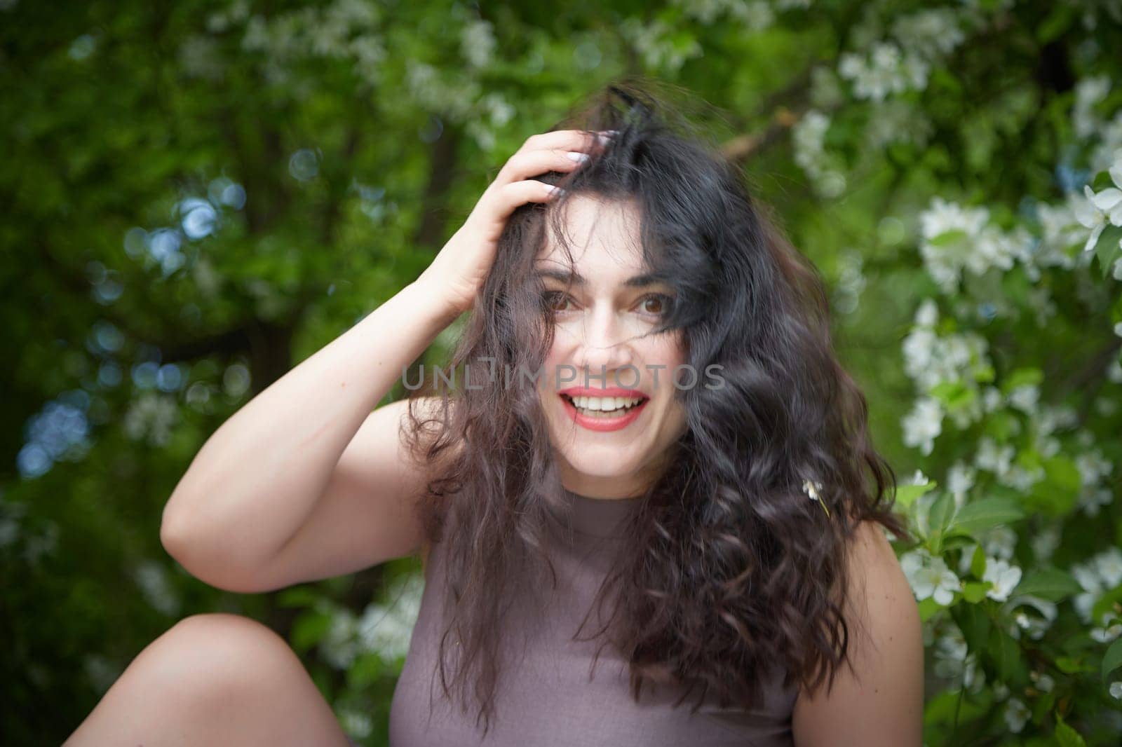 Joyous brunette woman near Blossoms of apple tree in a Spring Garden outdoors. The Concept of face and body care. The scent of perfume and tenderness