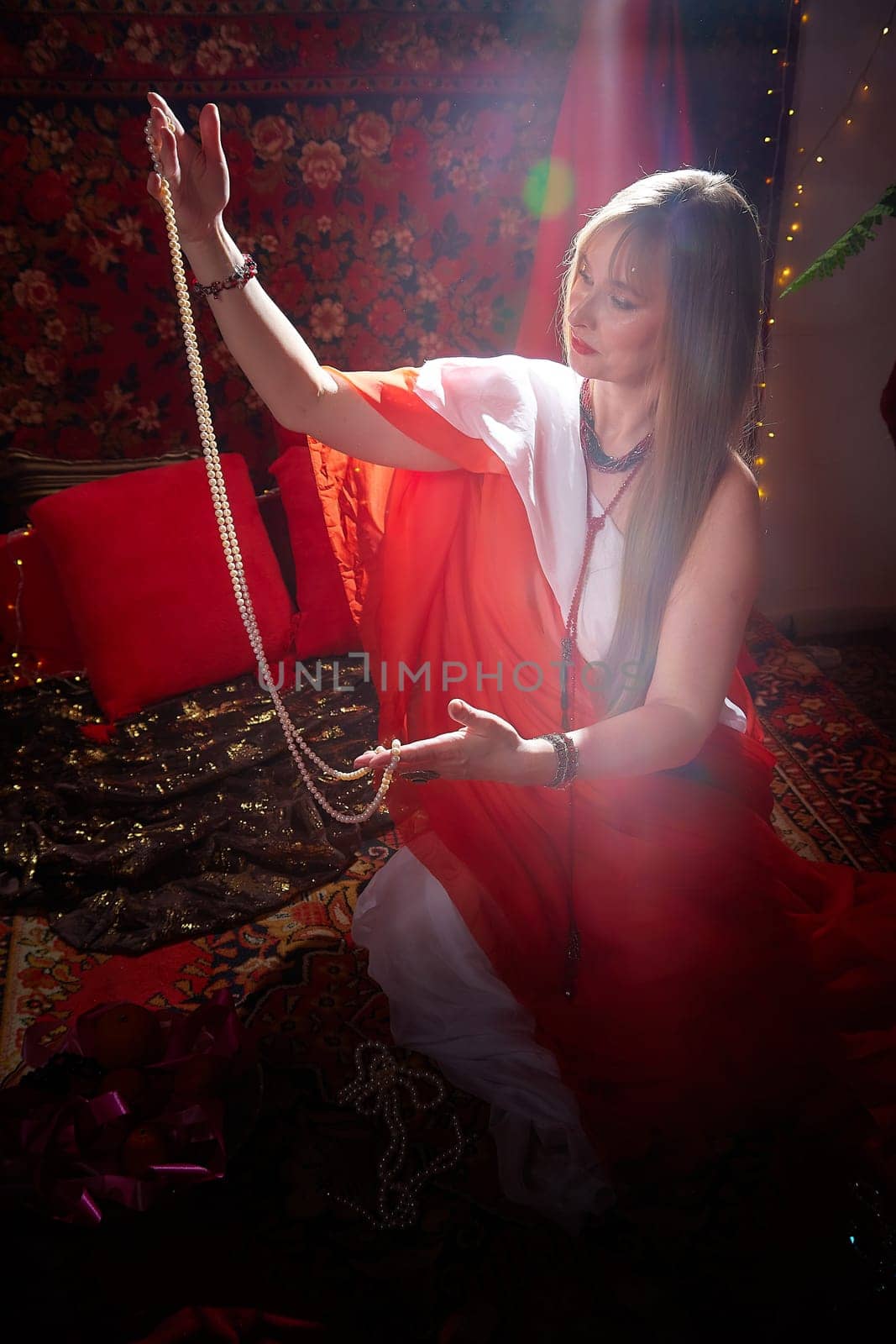 Beautiful European girl looking like Arab woman in red room with rich fabrics and carpets in sultan harem. Photo shoot of an oriental style odalisque. A model poses in sari as indian woman in india