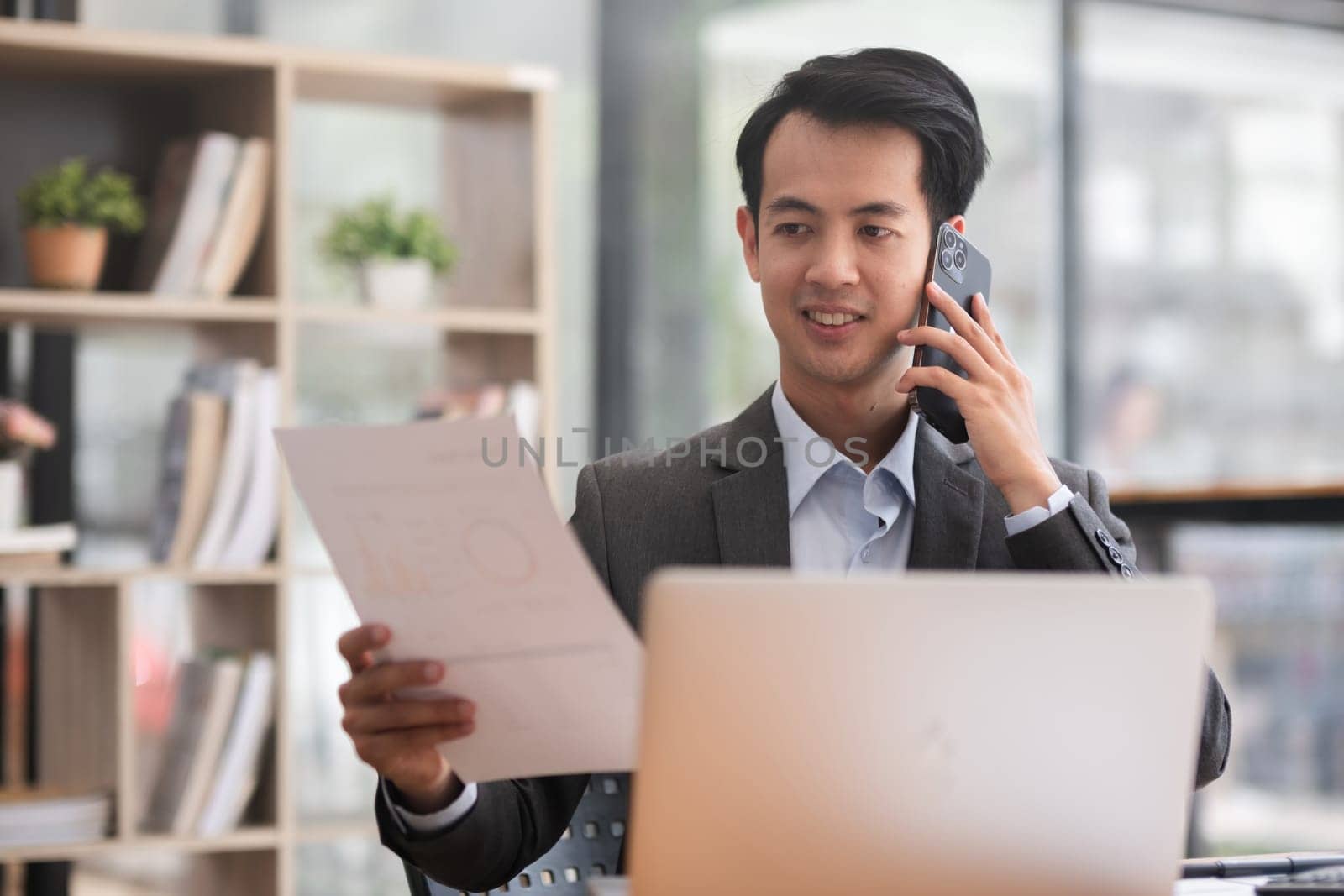 Young Asian man working on laptop in modern office Make telephone conversations, analyze accounting, report real estate investment information..