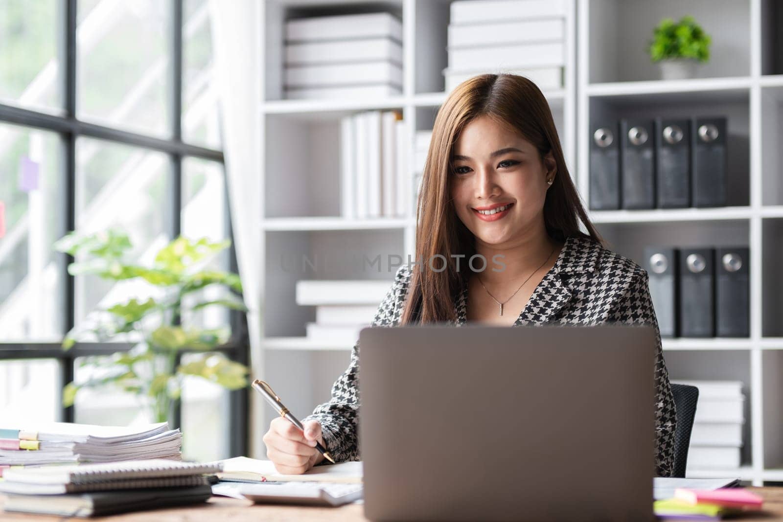 Beautiful accountant sitting working with laptop calculating financial and tax figures for company on desk in living room. by wichayada