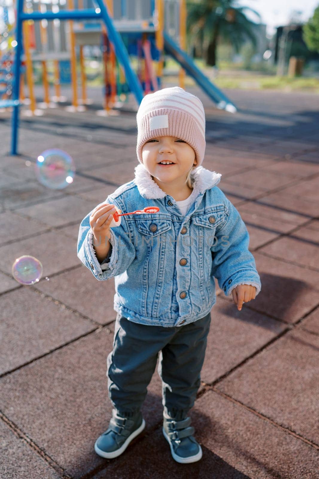 Little smiling girl blowing soap bubbles on the playground. High quality photo