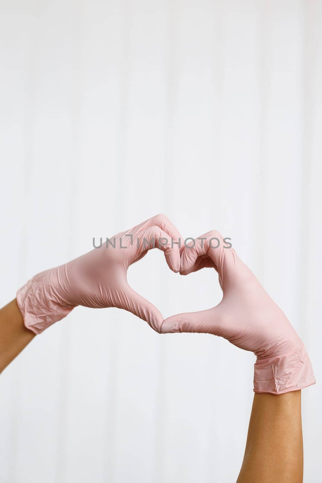 Hands with gloves making heart shape symbolize love or support to medical team. Person in pink latex gloves showing heart gesture against white background, closeup on hands by uflypro
