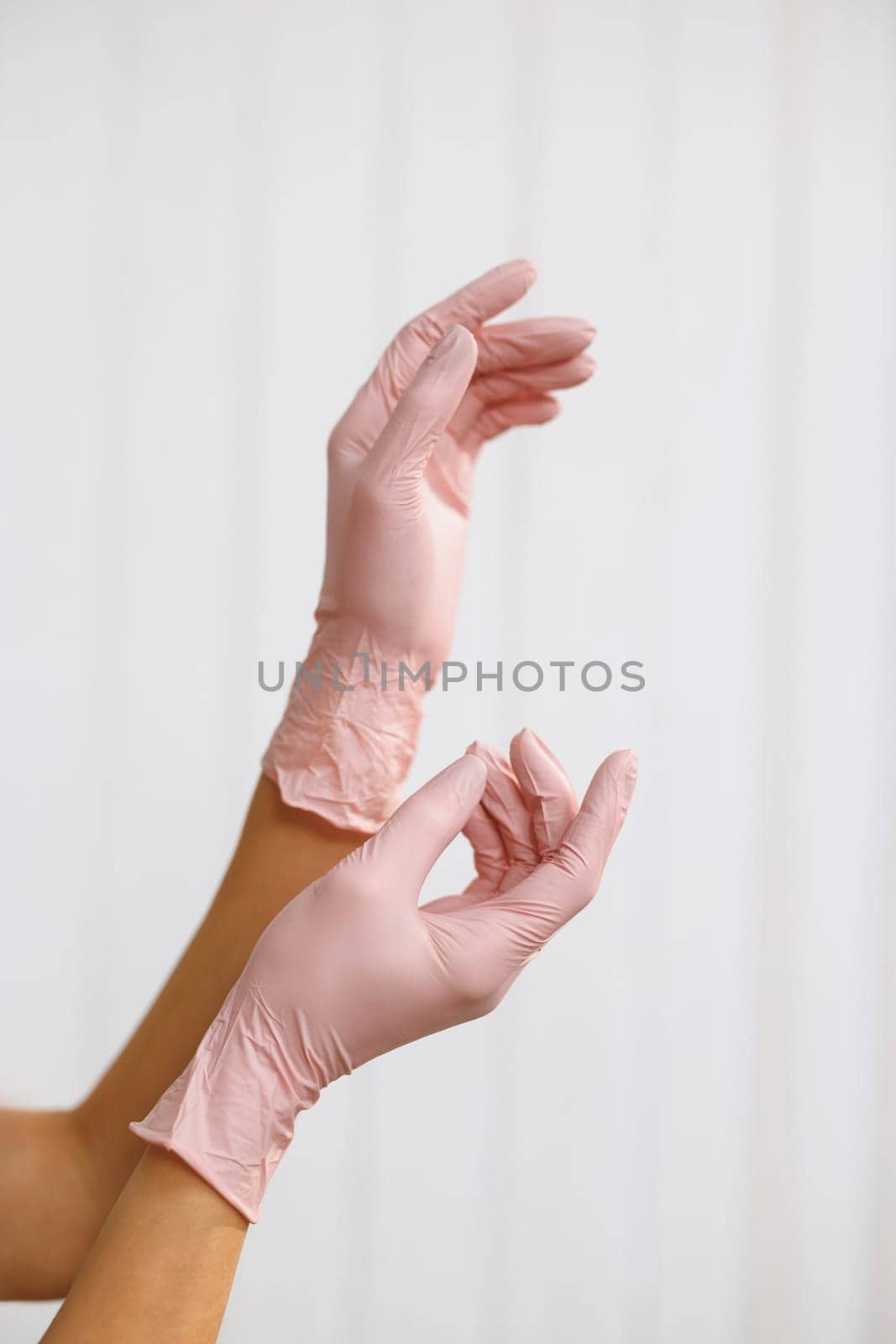 Hands wearing a pink latex glove. Two hands of a woman wearing gloves on a white background. Prevention of viral diseases by uflypro