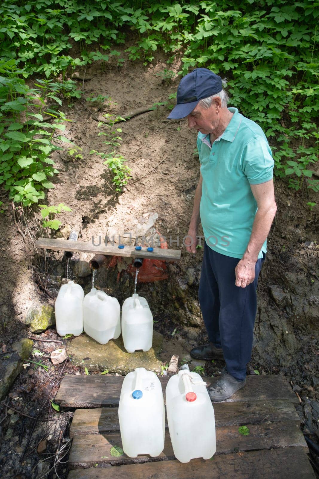 middle aged man fills canisters with clean fresh water from a spring, an underground source of drinking mineral water, high quality photo. by KaterinaDalemans