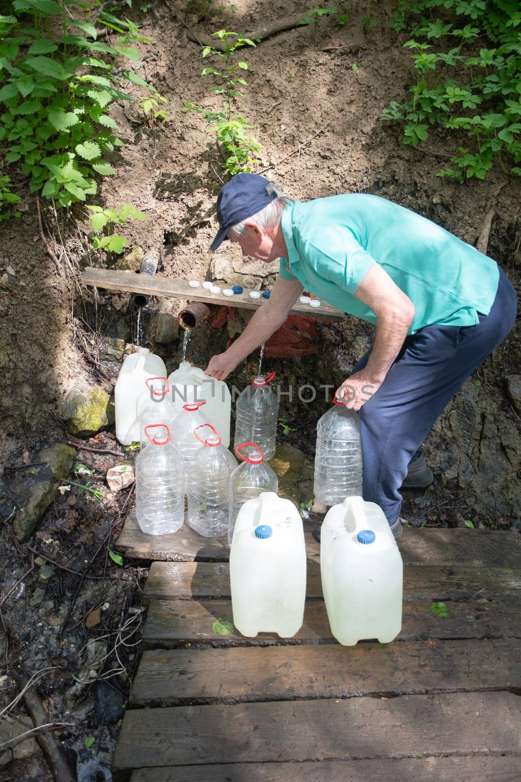 middle aged man fills canisters with clean fresh water from a spring, an underground source of drinking mineral water, high quality photo.