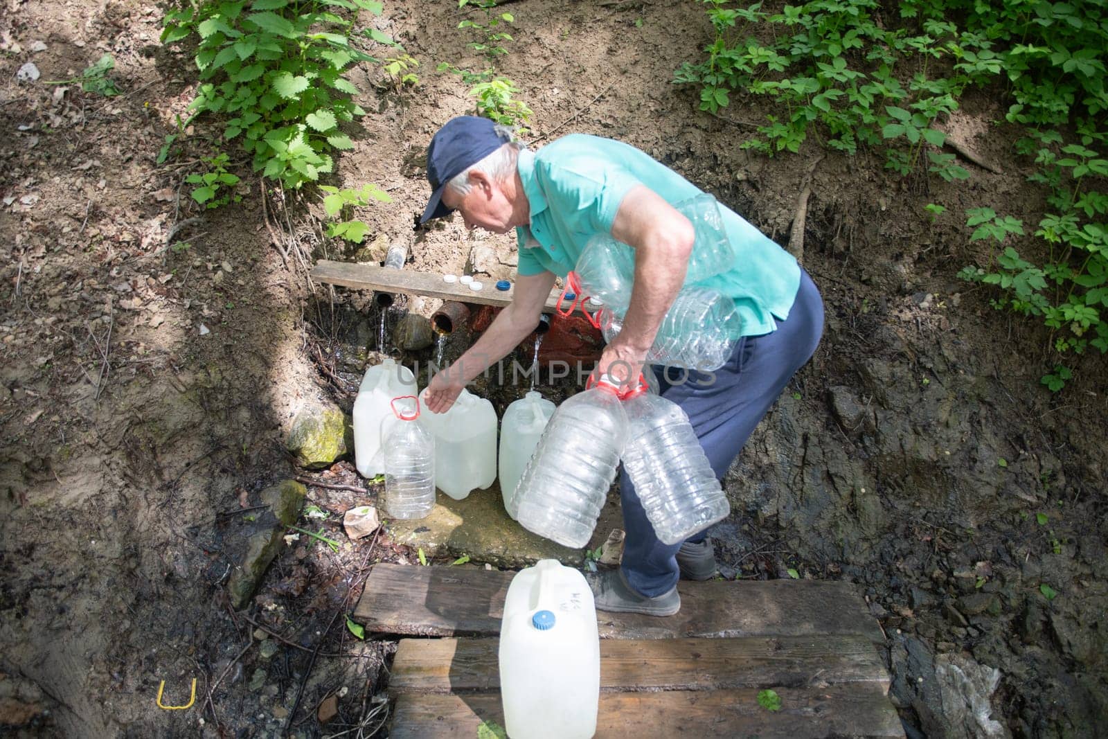 middle aged man fills canisters with clean fresh water from a spring, an underground source of drinking mineral water, high quality photo.