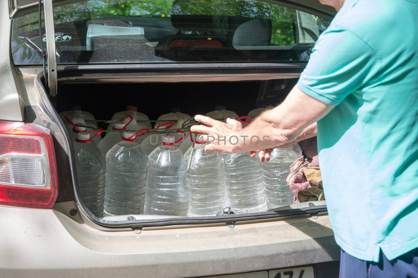 male volunteer loads many five-liter bottles of clean drinking water into the trunk to help victims of a natural disaster. High quality photo