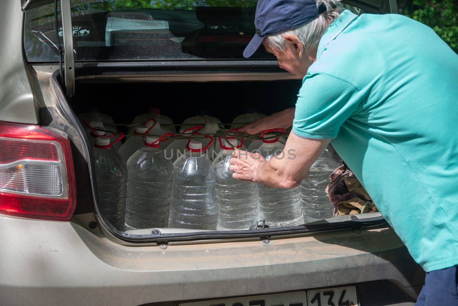 male volunteer loads many five-liter bottles of clean drinking water into the trunk to help victims of a natural disaster by KaterinaDalemans