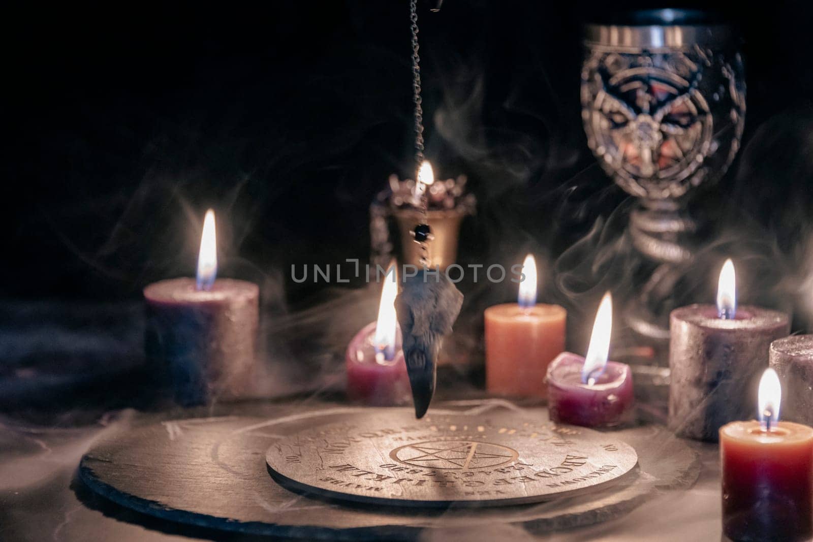 An eerie occult ritual setup featuring lit candles, a mystical symbol on slate, and a ceremonial goblet in a dark, moody setting. by jbruiz78