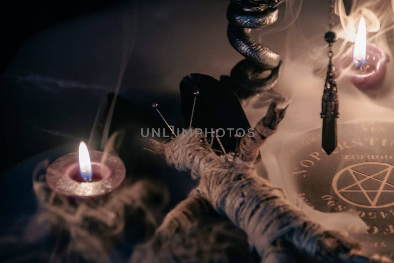 A haunting occult setup featuring a pendulum, mystical symbols, candles, a voodoo doll, and a ritual goblet amidst swirling smoke