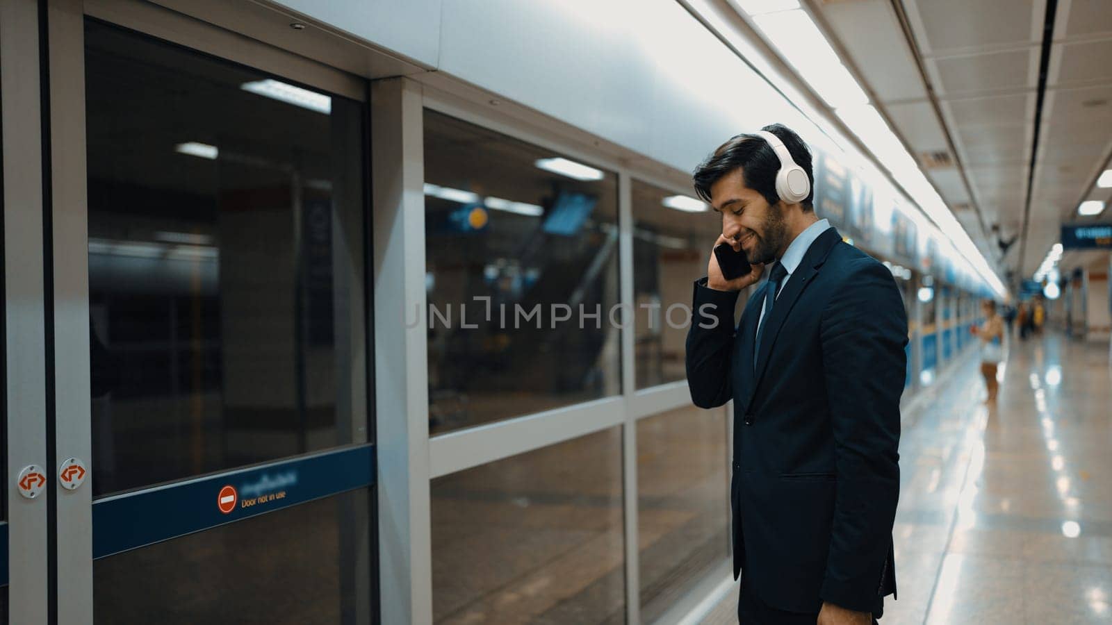 Business man calling phone while wearing headphone at train station. Exultant. by biancoblue