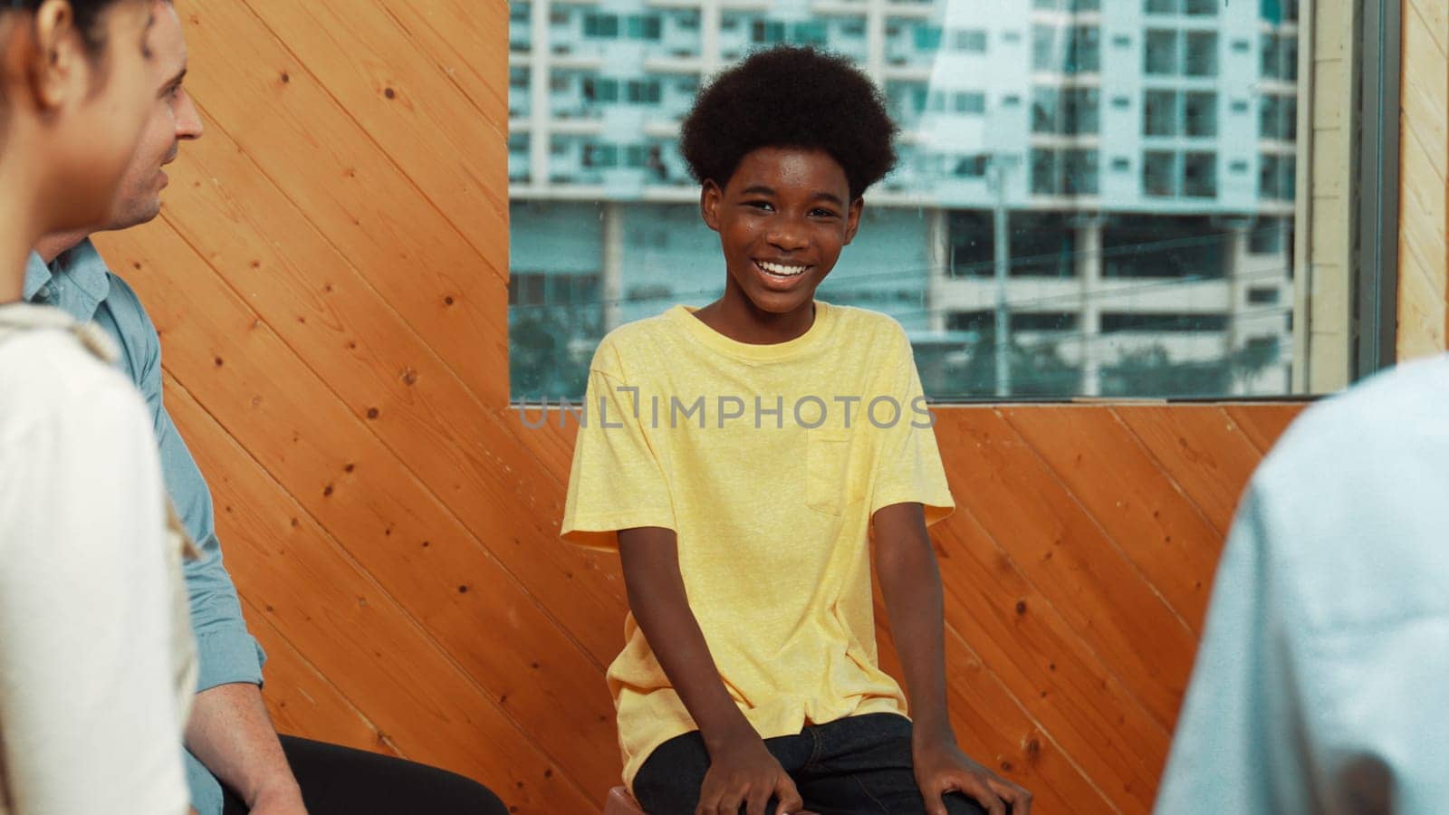 Smiling african boy sitting in circle while listening diverse friend sharing idea in group therapy with trust. Highschool student thinking and learning about mental health problem. Edification.