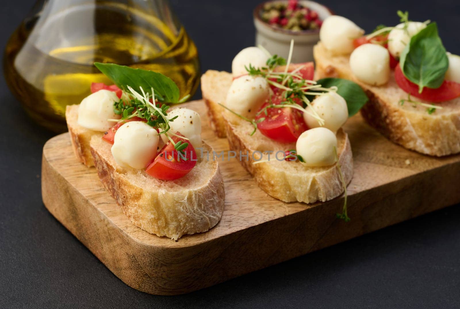 Round mozzarella, cherry tomatoes and microgreens on a piece of white bread, black table