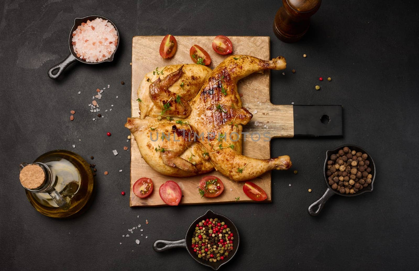 Whole fried chicken with spices on a wooden board on a black table by ndanko