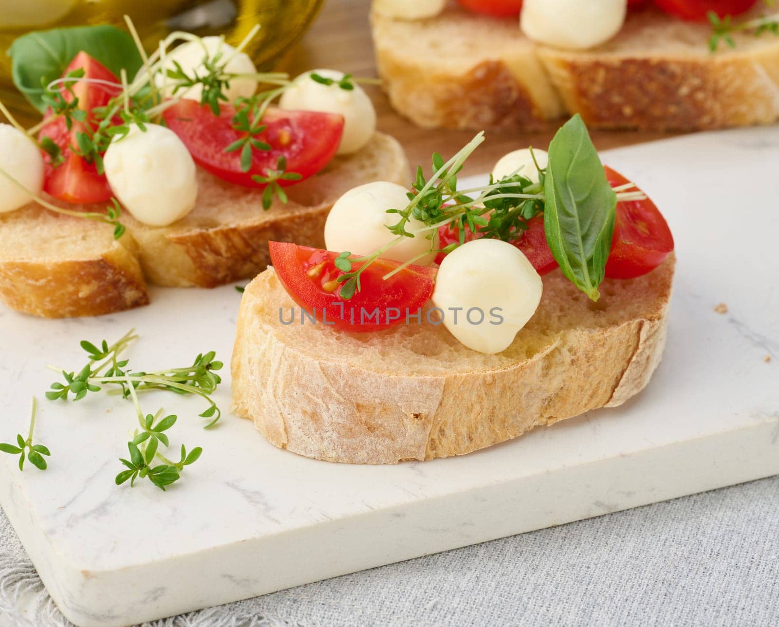 Round mozzarella, cherry tomatoes and microgreens on a piece of white bread, close up