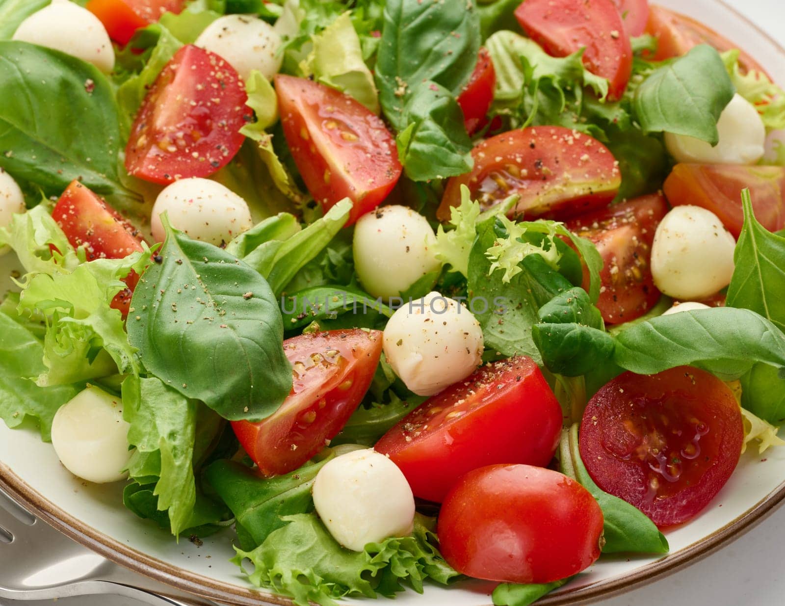 Salad with mozzarella, cherry tomatoes and green lettuce in a white round plate, close up