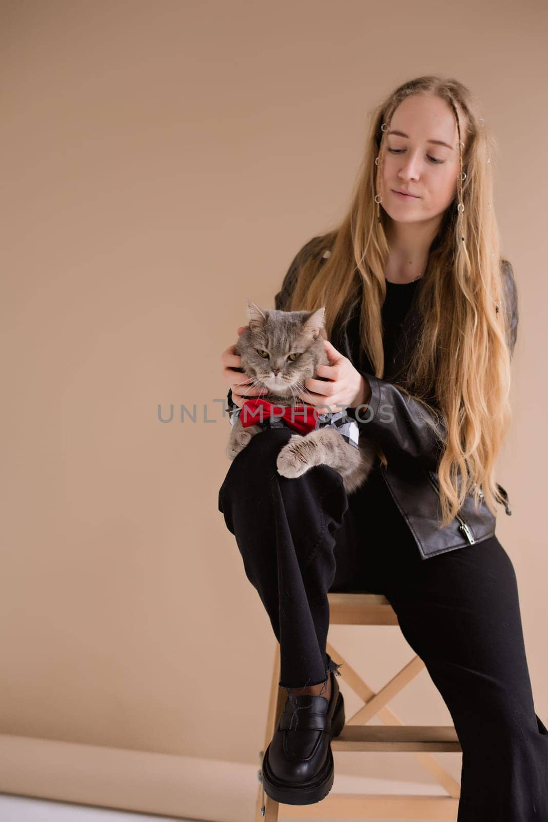 A woman natural blonde long hair smiling in a black clothes, sitting on photo studio. girl with pet scottish straight cat. portrait , vertical,