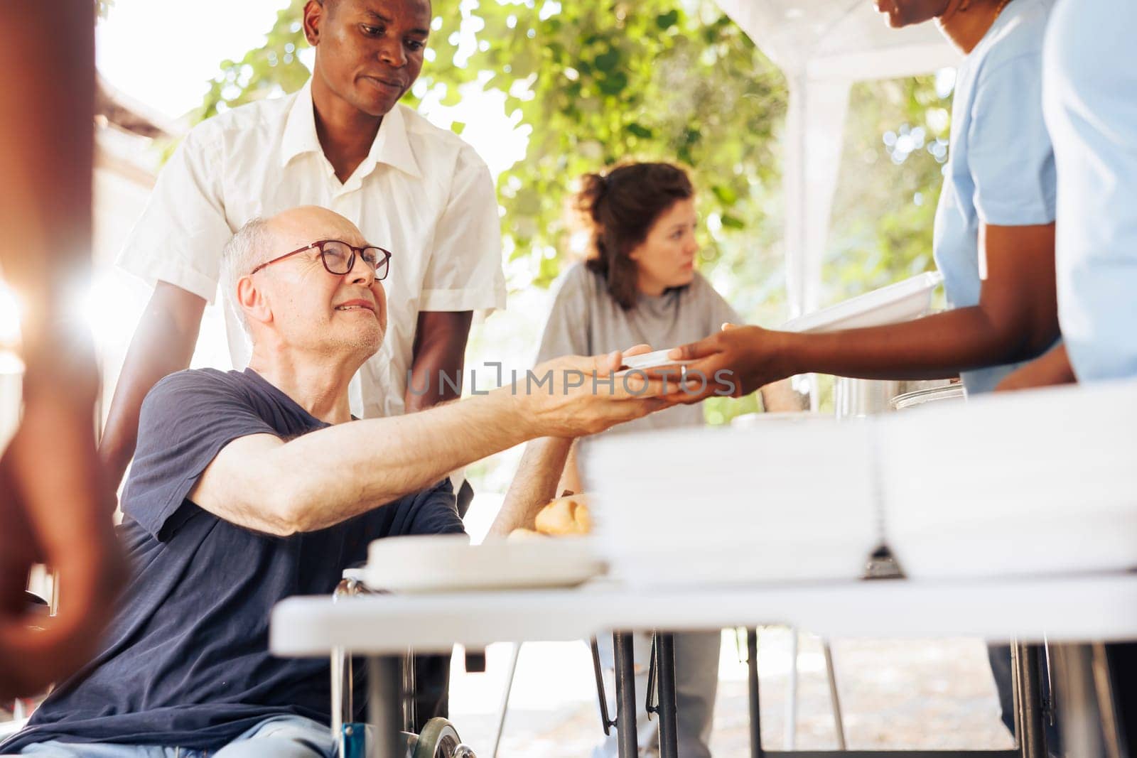 Charitable organisation gives assistance and free meals to homeless individuals, demonstrating dedication to fighting hunger and poverty. Volunteers provide a warm food to caucasian wheelchair user.