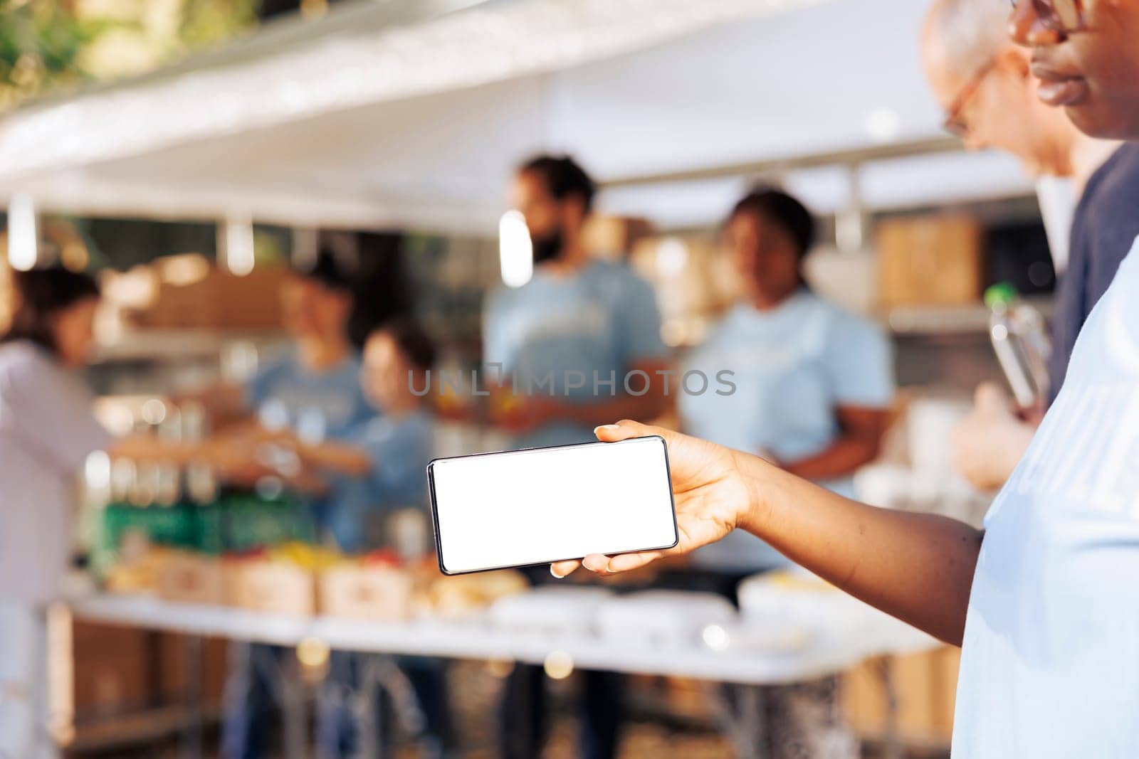 Black woman holding a cellphone with isolated mockup template for custom messages related to charity. African american female volunteers grasping digital device with blank white screen display.