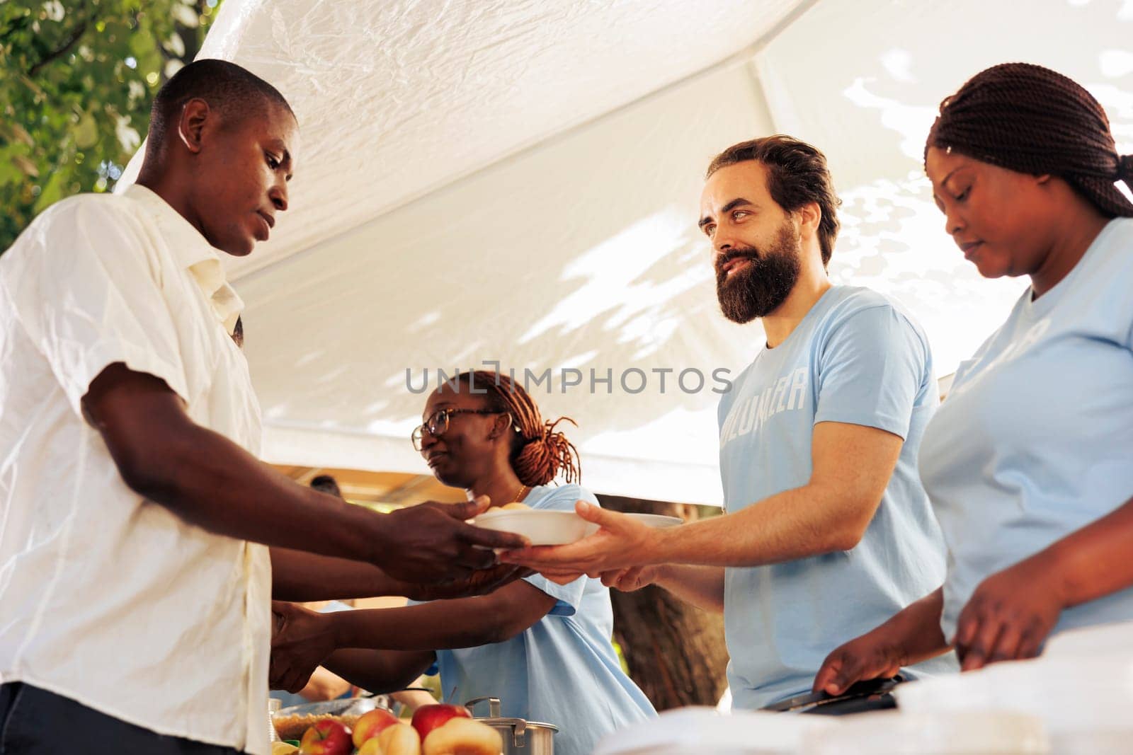 Interracial group in support of hunger relief volunteering in distribution of essential items and free food to needy and less fortunate individuals. Poor and homeless people receive humanitarian aid.