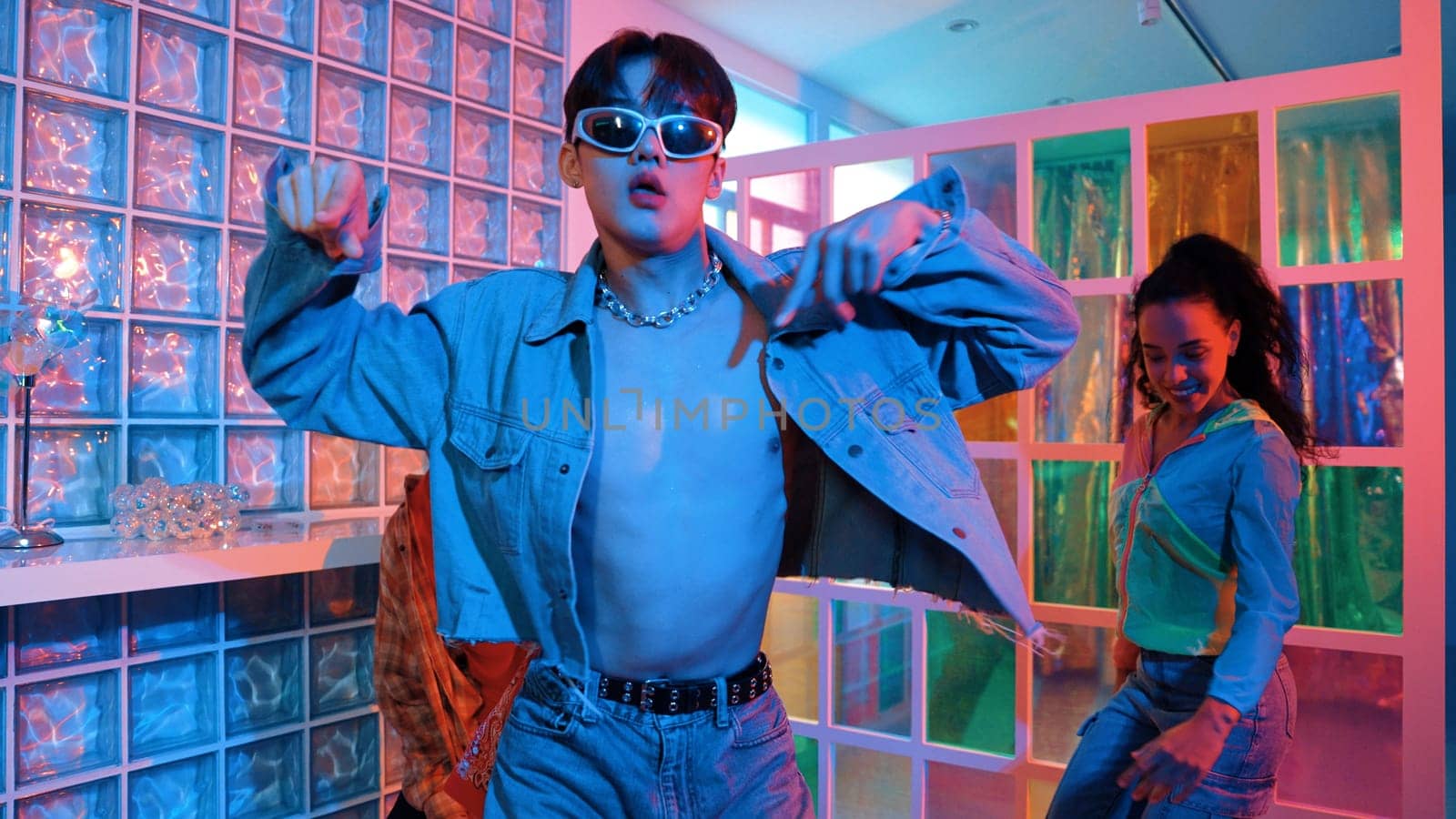 Asian man moving his arm while dancing with diverse team in neon light at night club. Happy dancer with stylish cloth moving along with multicultural hipster in lively mood at modern club. Regalement.