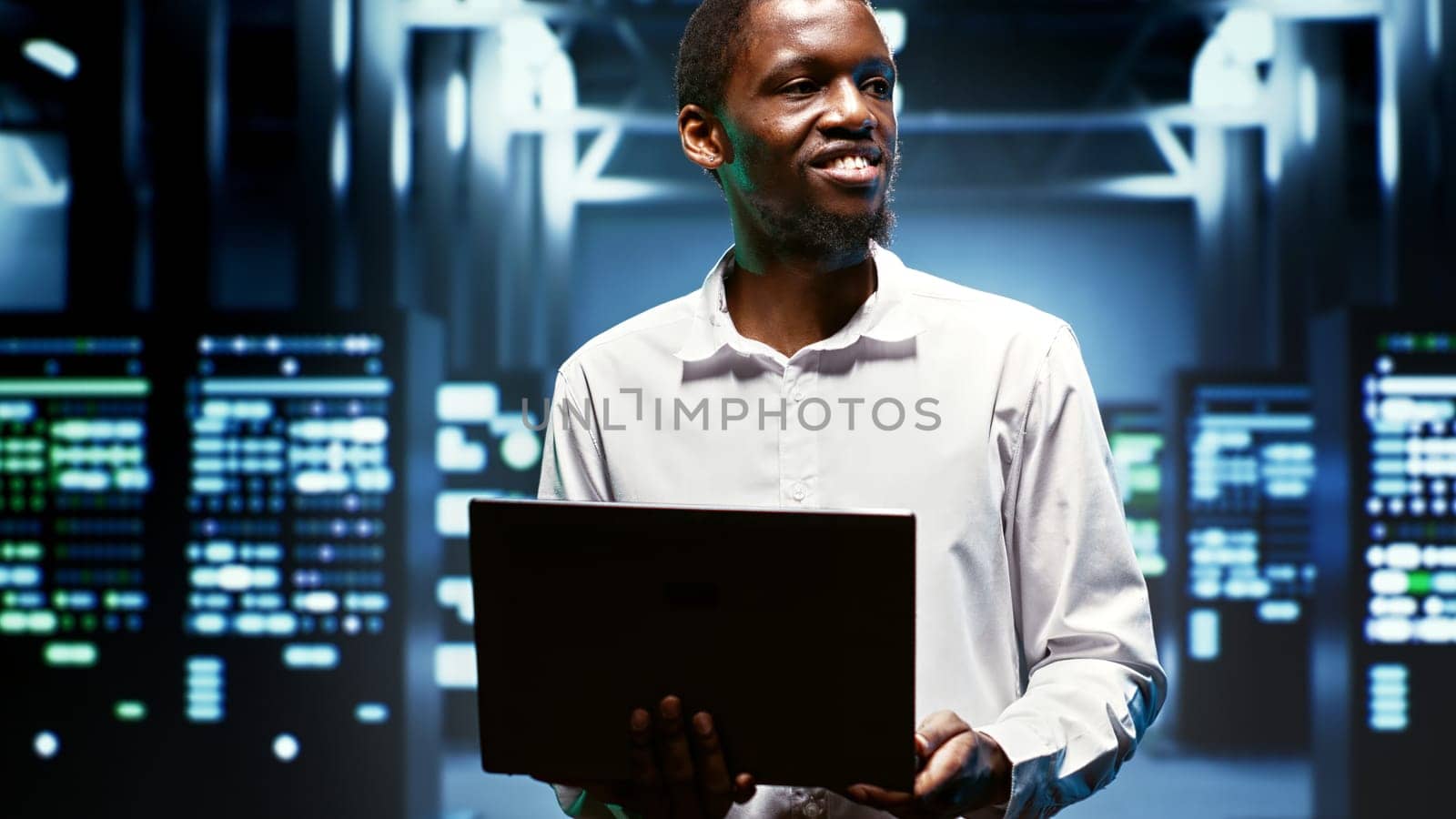 Cheerful system administrator using laptop to survey energy consumption across server rows components. Electrician making sure data center rigs temperature sensors are operating perfectly