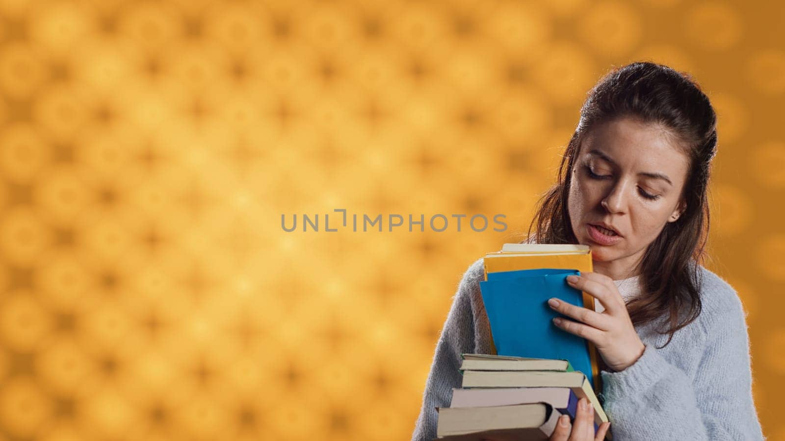 Excited woman browsing though pile of purchased books, picking what to read. Enthusiastic bookaholic person looking through stack of novels to spend leisure time with, studio background, camera A