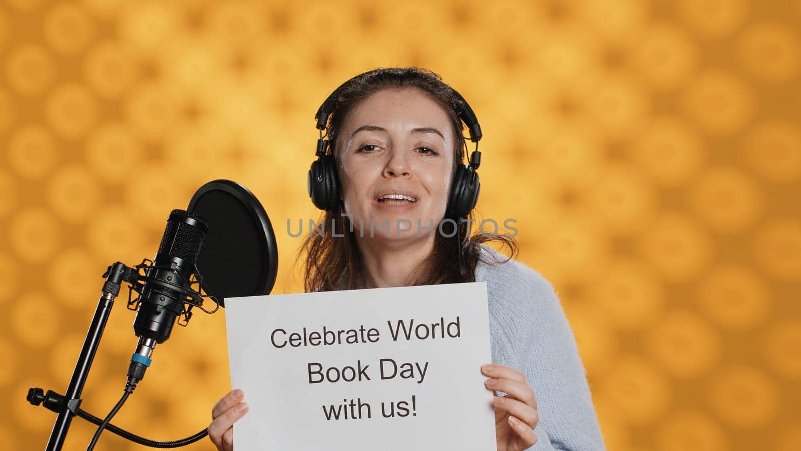 Smiling woman filming promotional video for world book day, isolated over studio background. Influencer promoting reading, gaining awareness for international global event, camera A