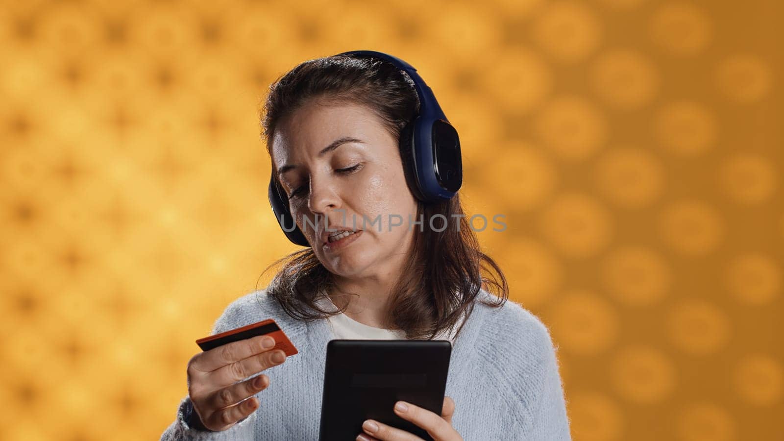 Woman buying electronic books for ereader using credit card, isolated over studio background. Bookworm listening music in headphones, purchasing ebooks, typing on tablet screen, camera A