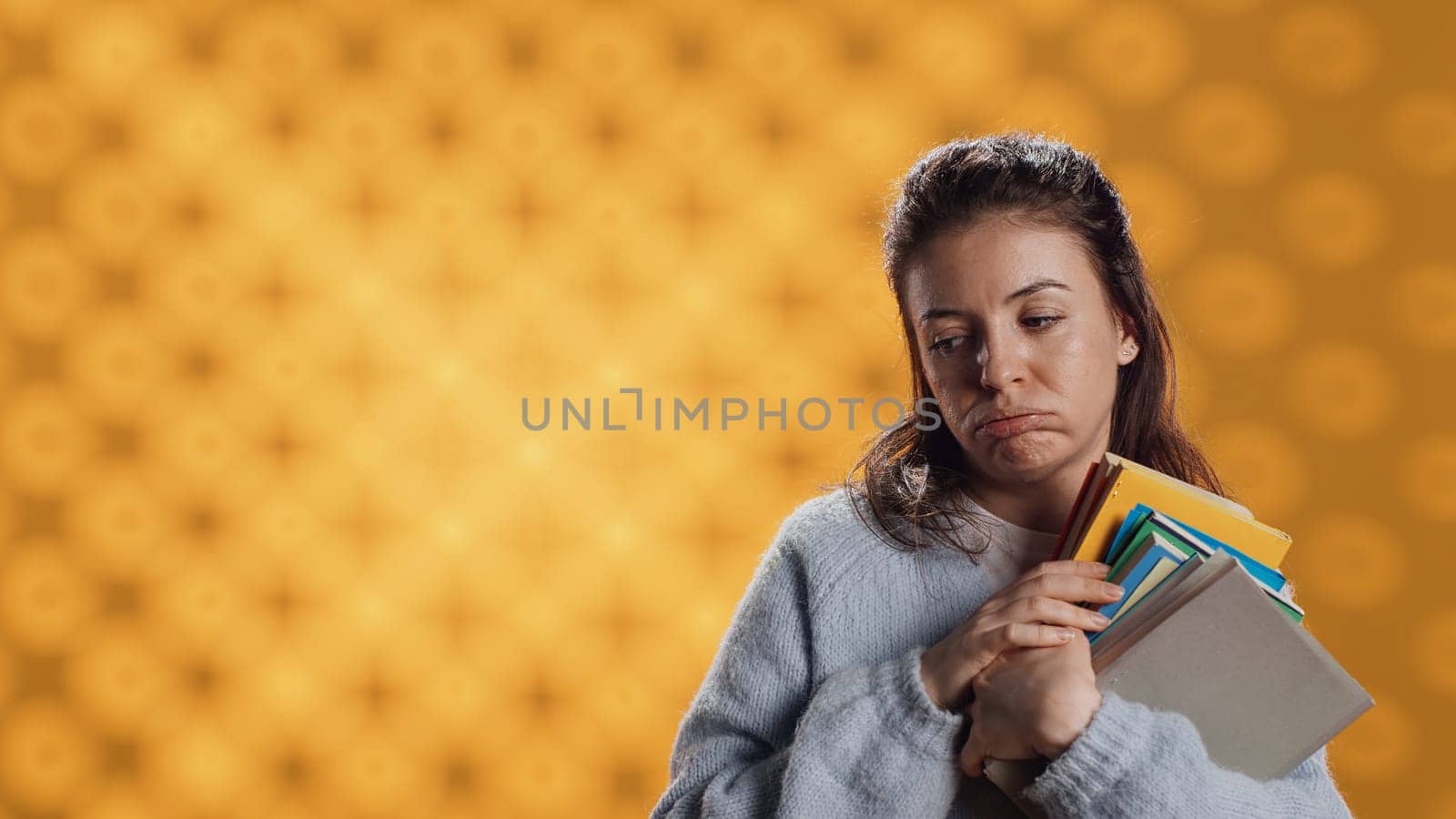Exhausted woman yawning, holding heavy stack of books needed for school exam, studio background. Student yearning for sleep, tired of learning from academic textbooks, camera A