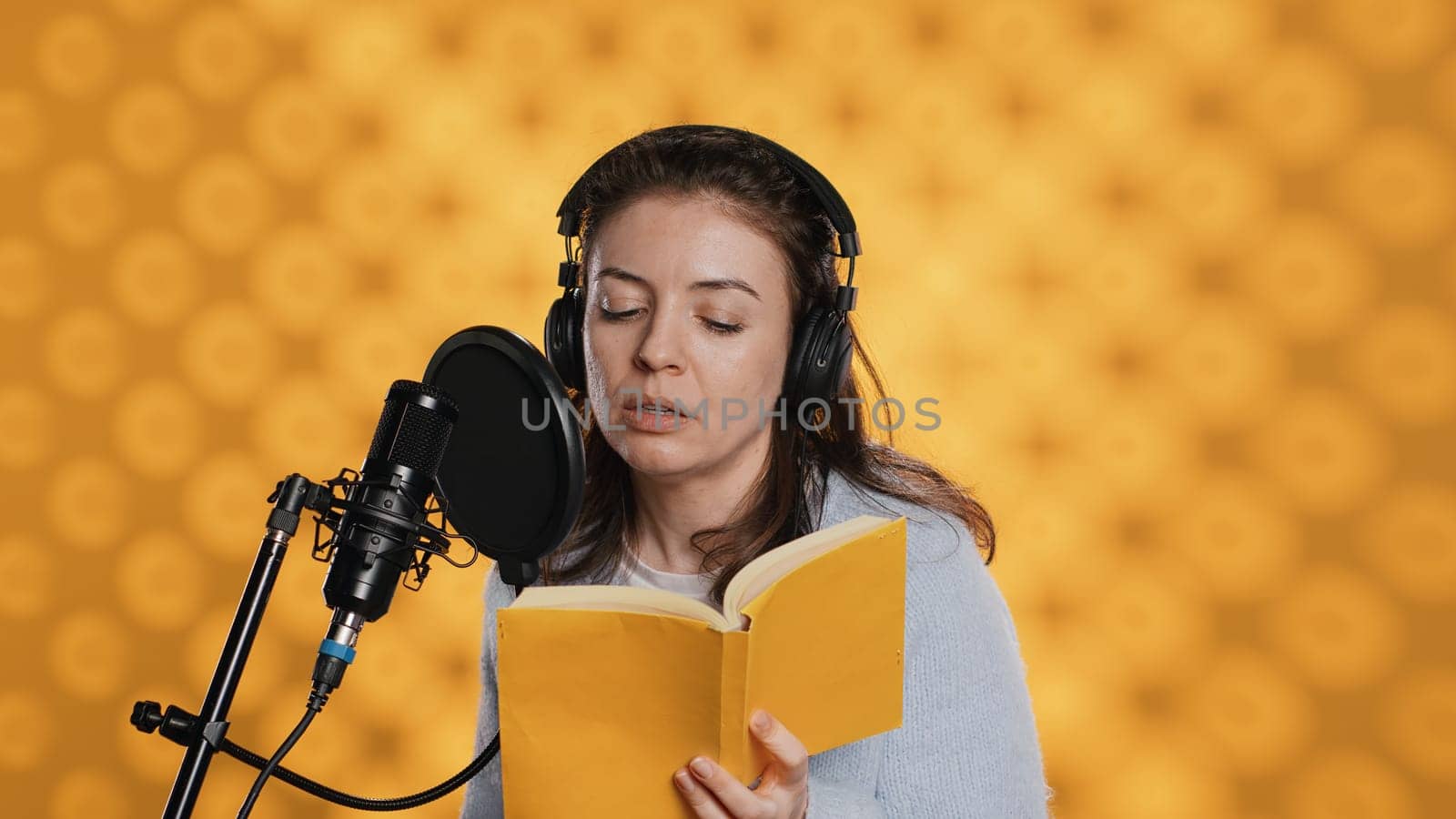 Narrator wearing headset reading aloud from book into mic, studio background by DCStudio