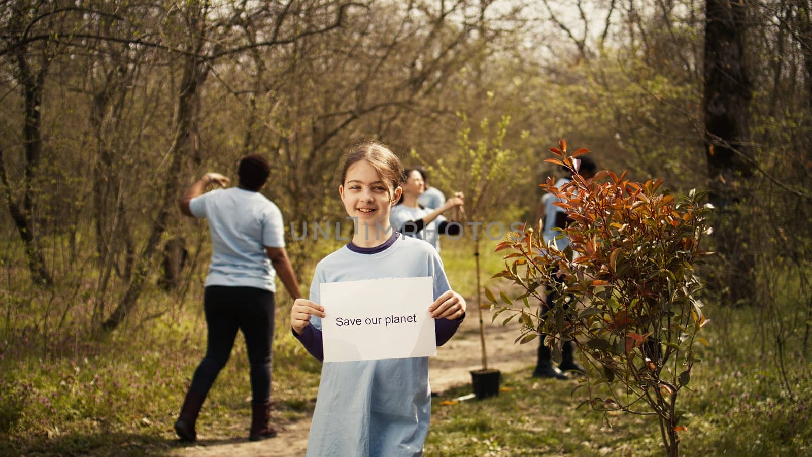 Portrait of sweet girl with save our planet poster against pollution and illegal dumping, volunteering to restore and preserve nature in the forest. Little child shows awareness sign. Camera B.