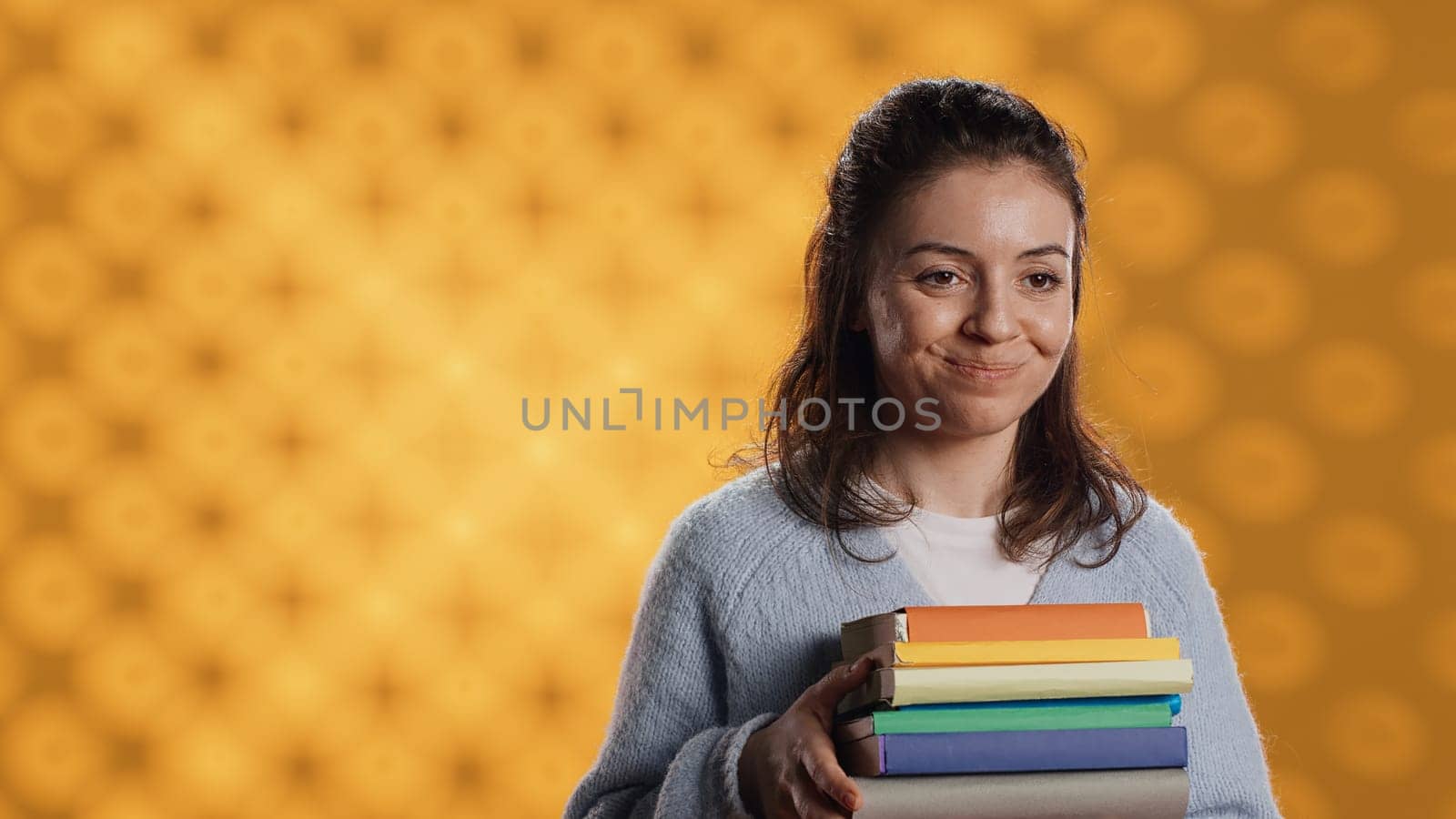 Portrait of smiling woman holding stack of books, doing salutation hand gesture by DCStudio