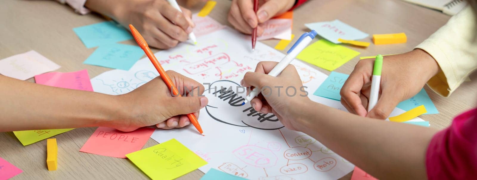 Professional startup group share creative marketing idea by using mind map. Young skilled business people brainstorm business plan while writing sticky notes. Focus on hand. Closeup. Variegated.