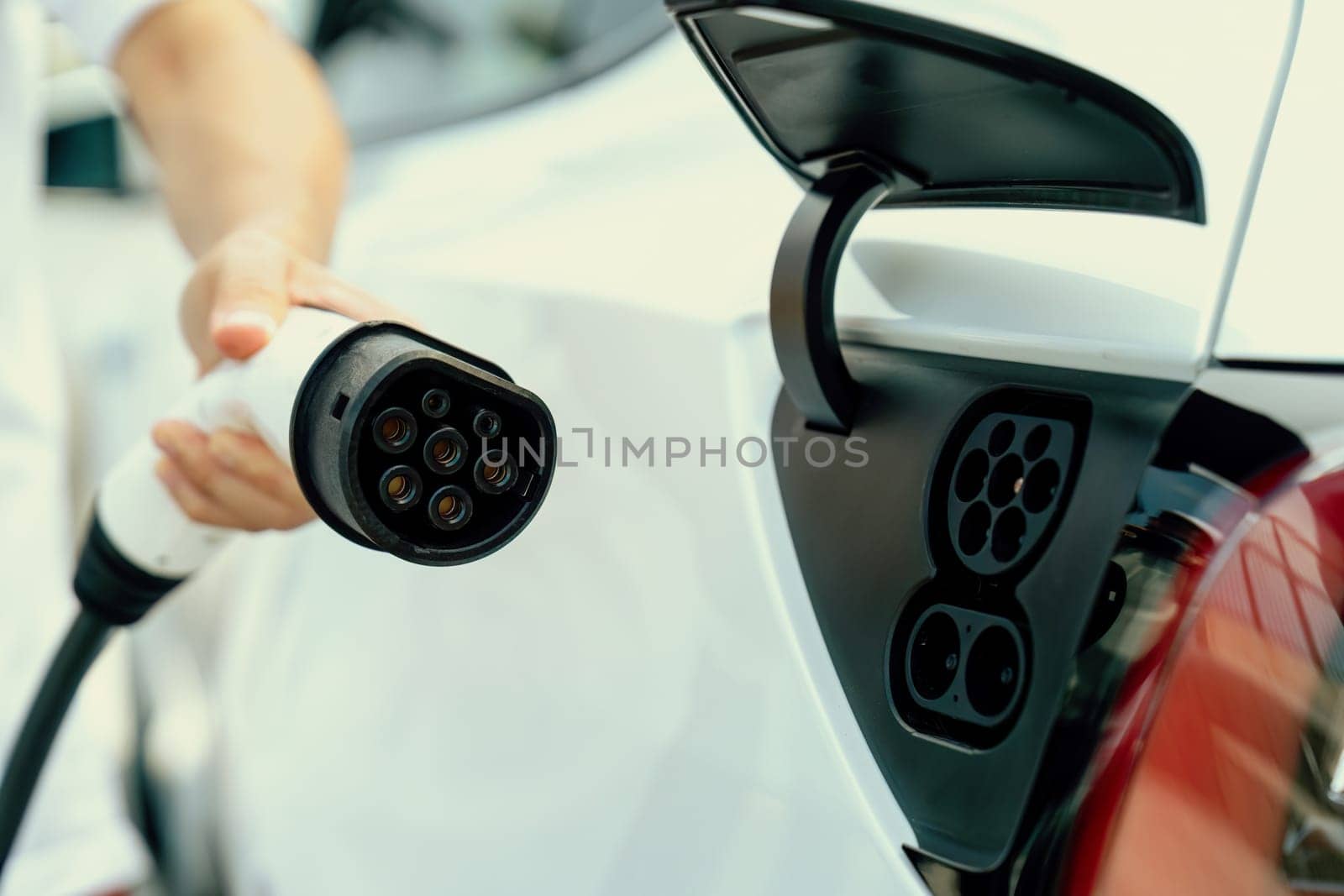 Hand insert EV charger plug into electric vehicle to recharge EV car. Perpetual by biancoblue