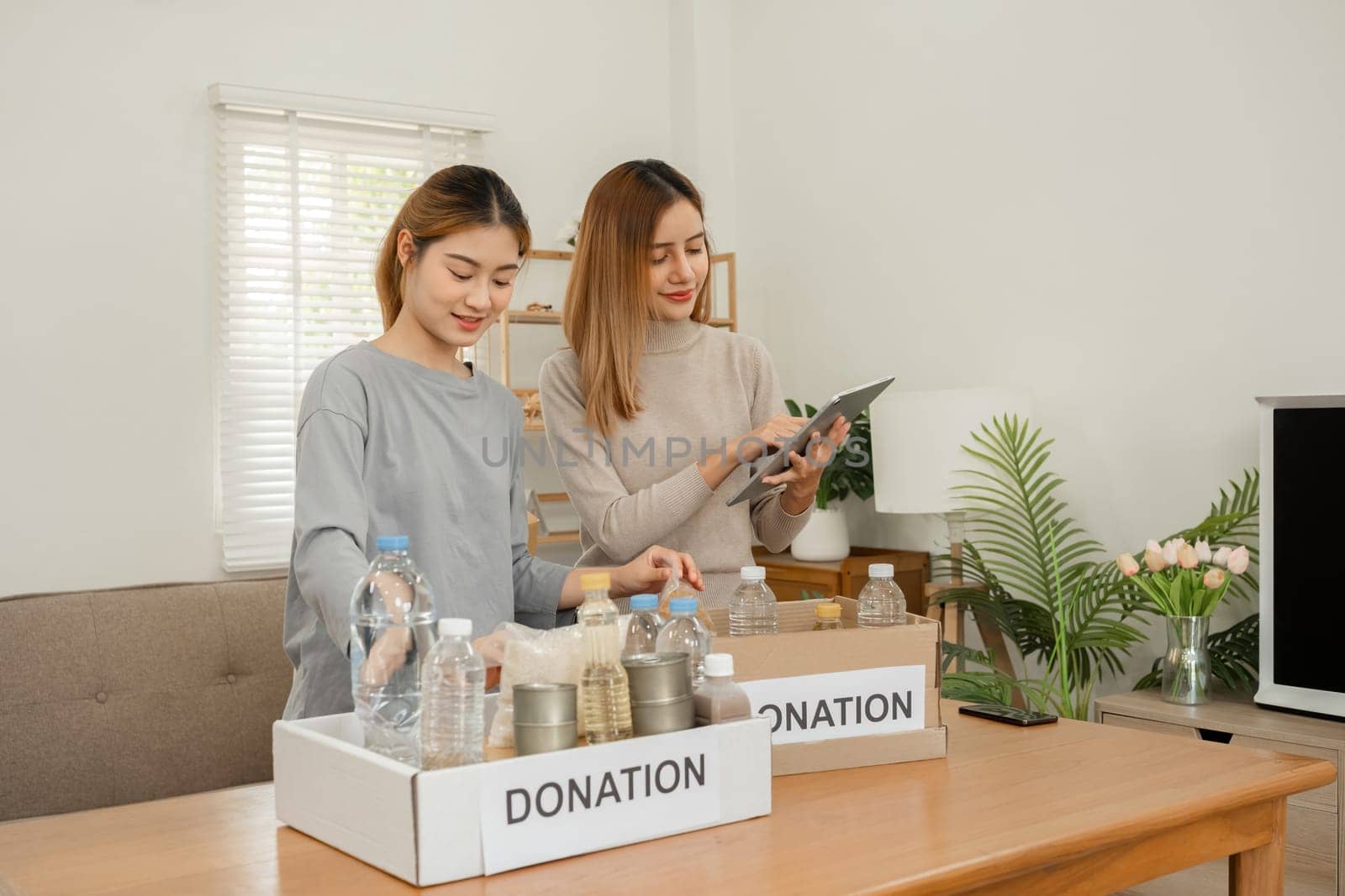 Two young female volunteers help pack food into donation boxes and prepare donation boxes to take to charities. by wichayada