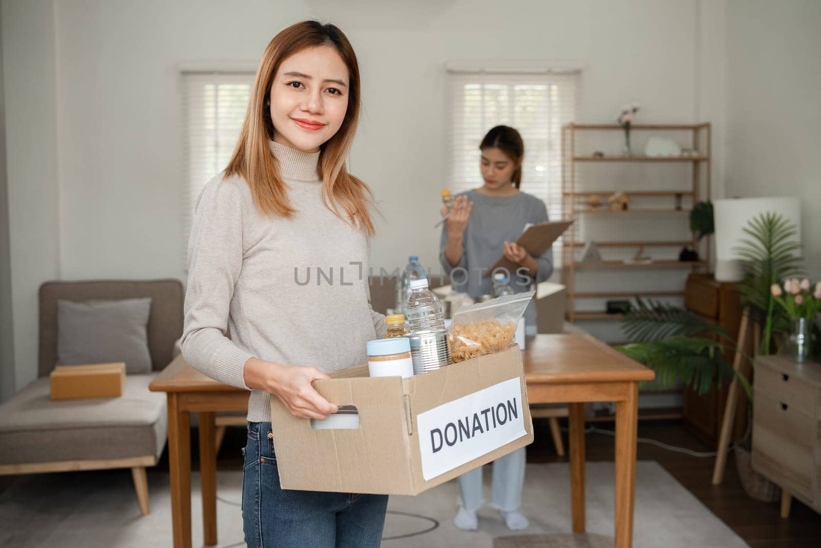 A beautiful female volunteer carries a donation box with canned food and food to donate to the Nothi Foundation. by wichayada