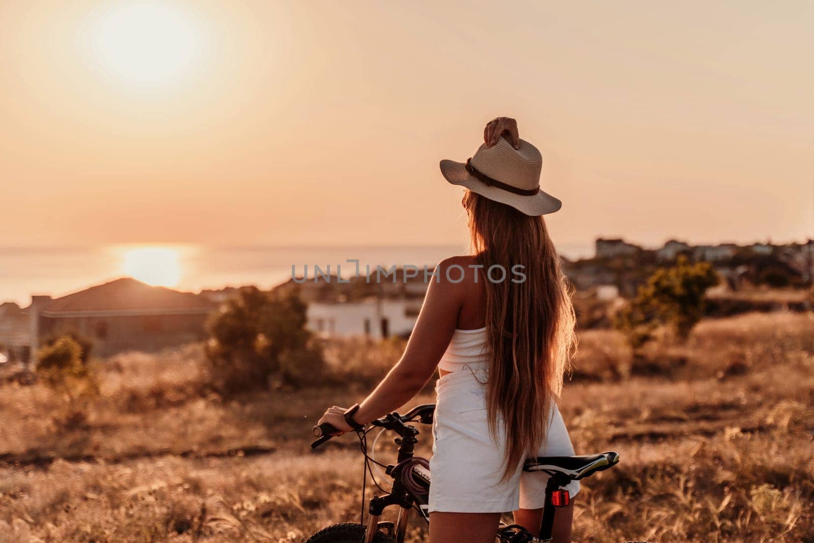 A woman cyclist on a mountain bike looking at the landscape sea. Adventure travel on bike. by Matiunina