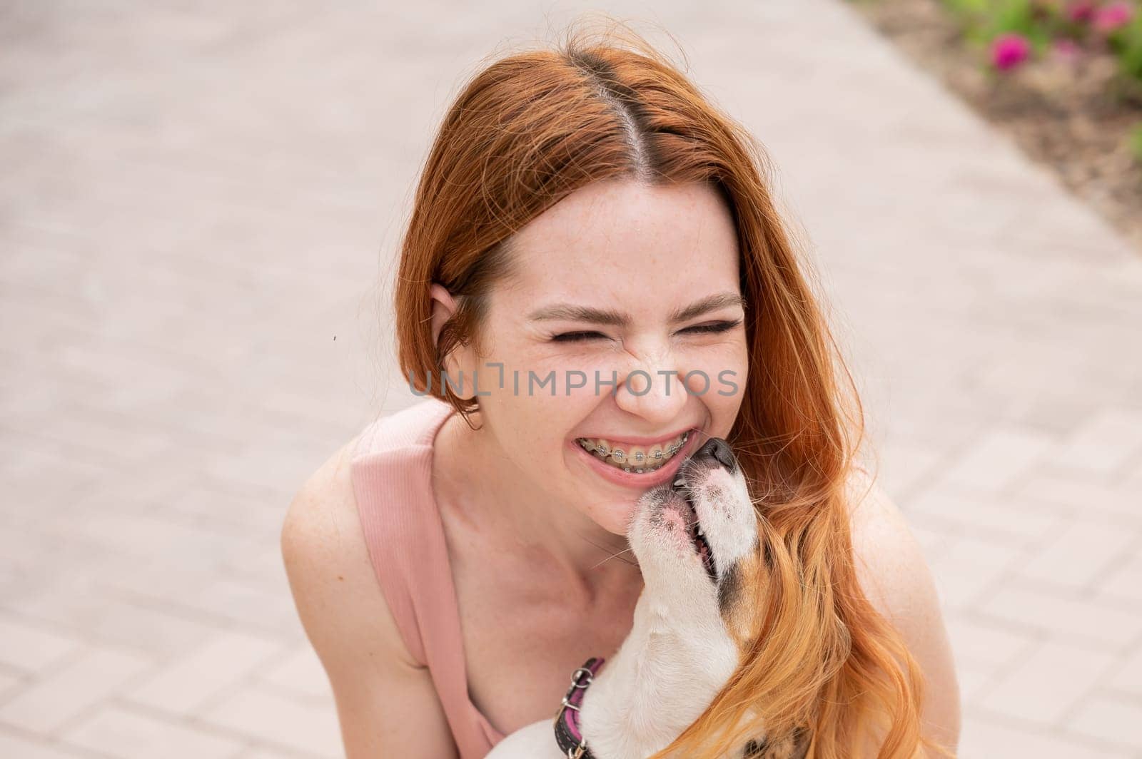 Dog jack russell terrier licks the owner in the face outdoors. Girl with braces on her teeth