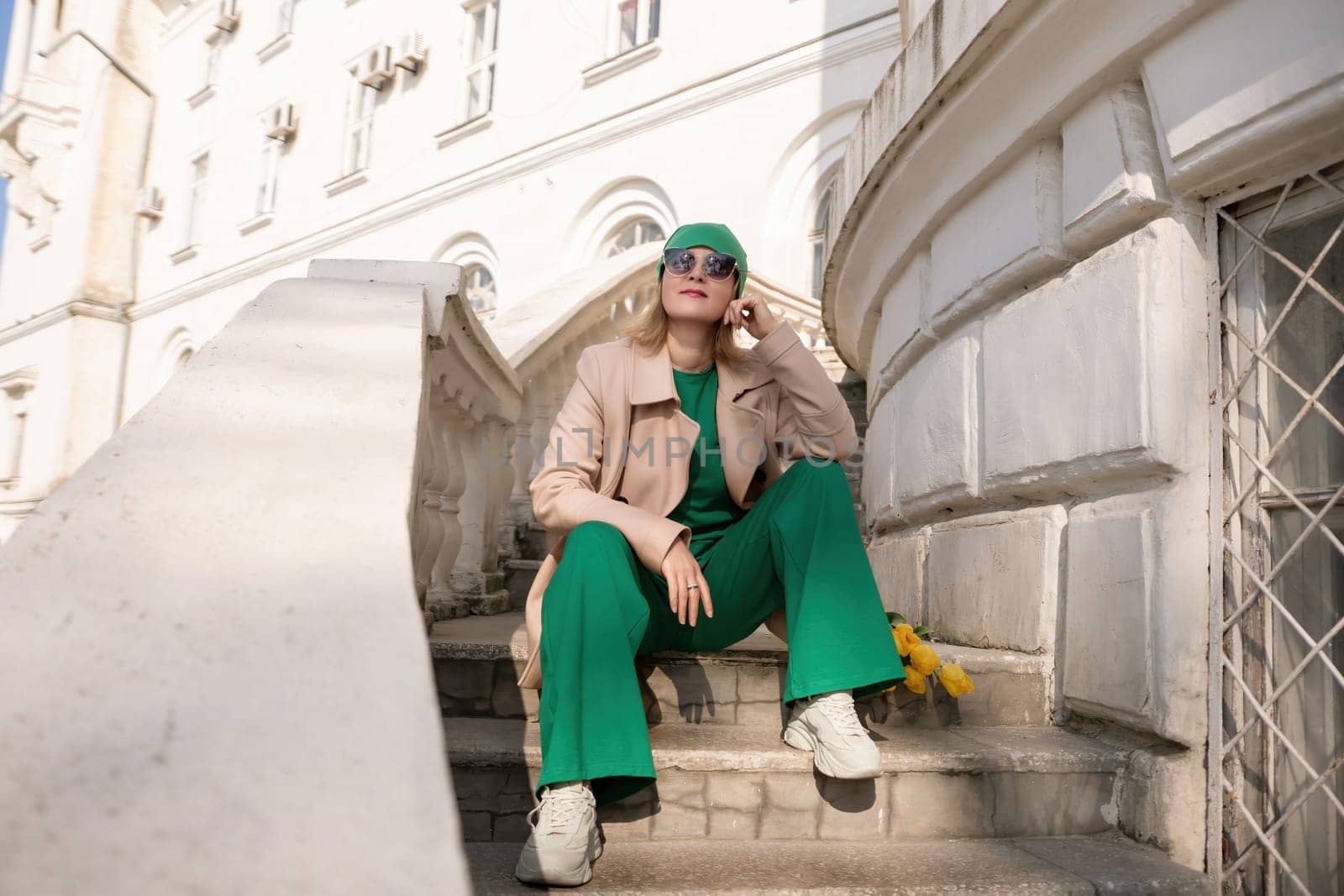 A woman in a green outfit is sitting on a set of stairs. She is wearing a green hat and sunglasses. by Matiunina