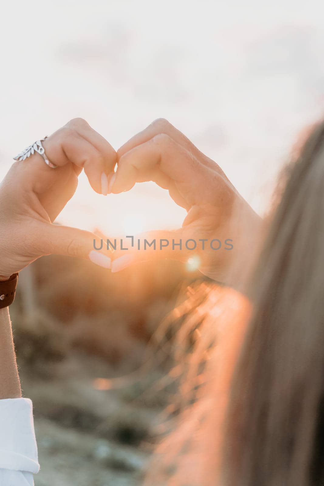 A woman's hand is holding a heart shape, with the sun shining on it. Concept of love and warmth, as the sun symbolizes happiness and positivity. The heart shape represents the bond between two people. by panophotograph
